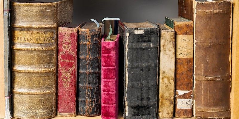 A row of old books are lined up on a shelf.