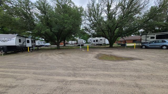 A lot of rvs are parked in a gravel lot surrounded by trees.