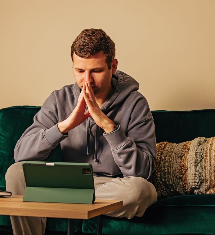 A man is sitting on a couch looking at a tablet