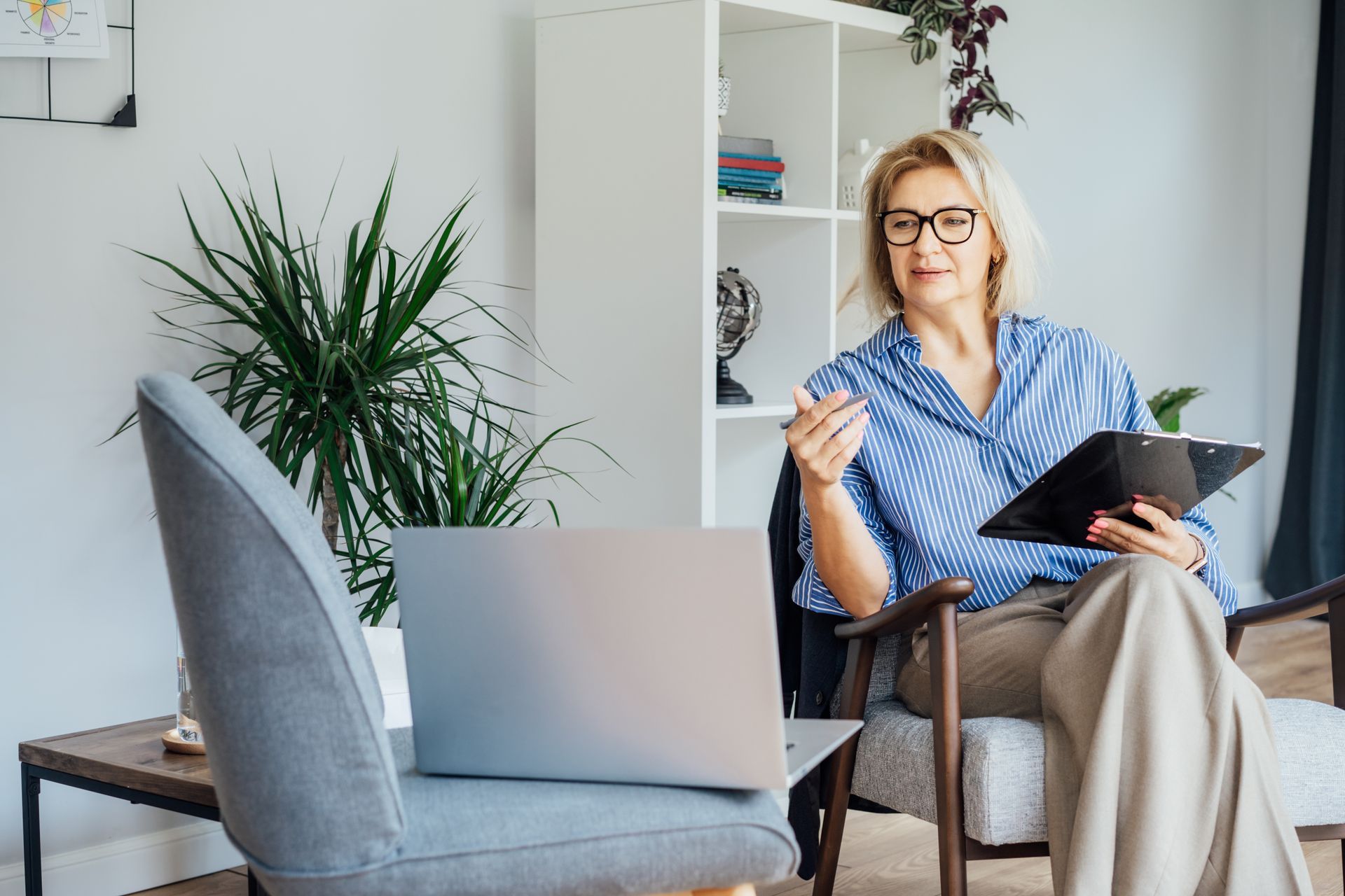 A woman is sitting in a chair with a laptop and a clipboard.