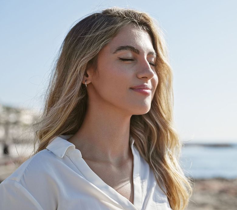 A woman is standing on a beach with her eyes closed.