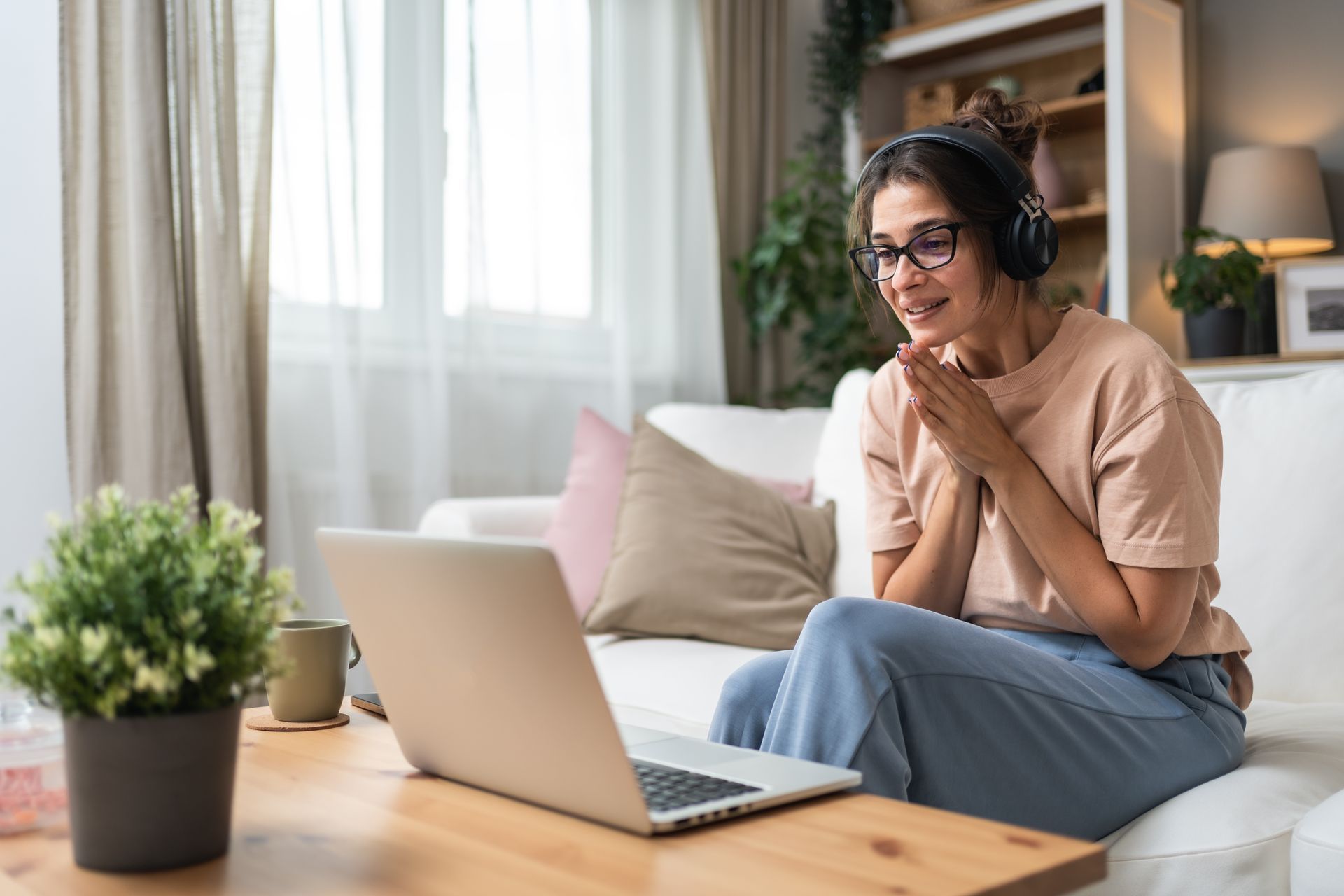 A woman is sitting on a couch using a laptop computer while wearing headphones.