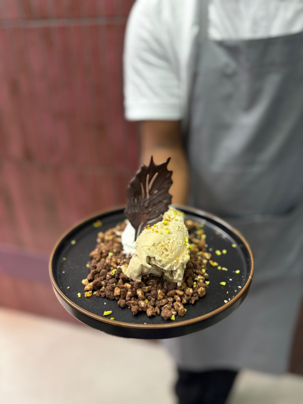 Chef che tiene in mano un piatto di dessert con gelato, crumble di cioccolato e guarnizione.