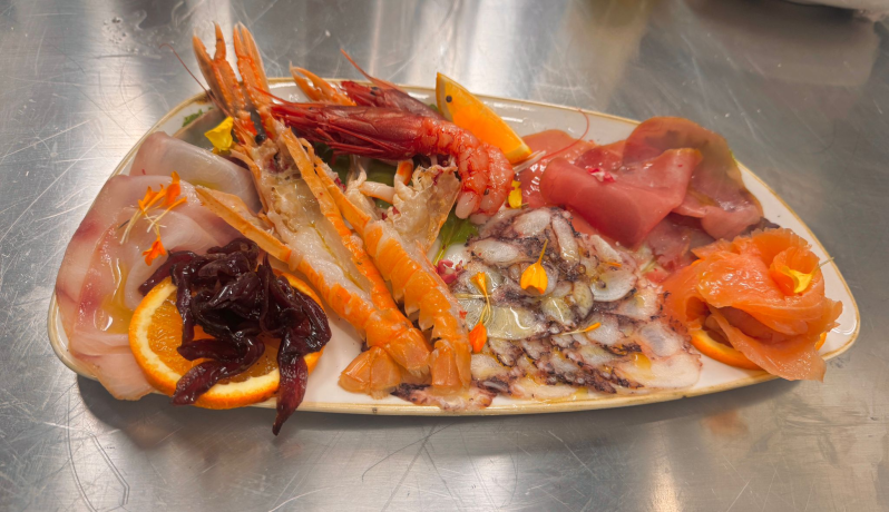 Piatto di frutti di mare con gamberi, pesce e polpo, guarnito con fette d'arancia.