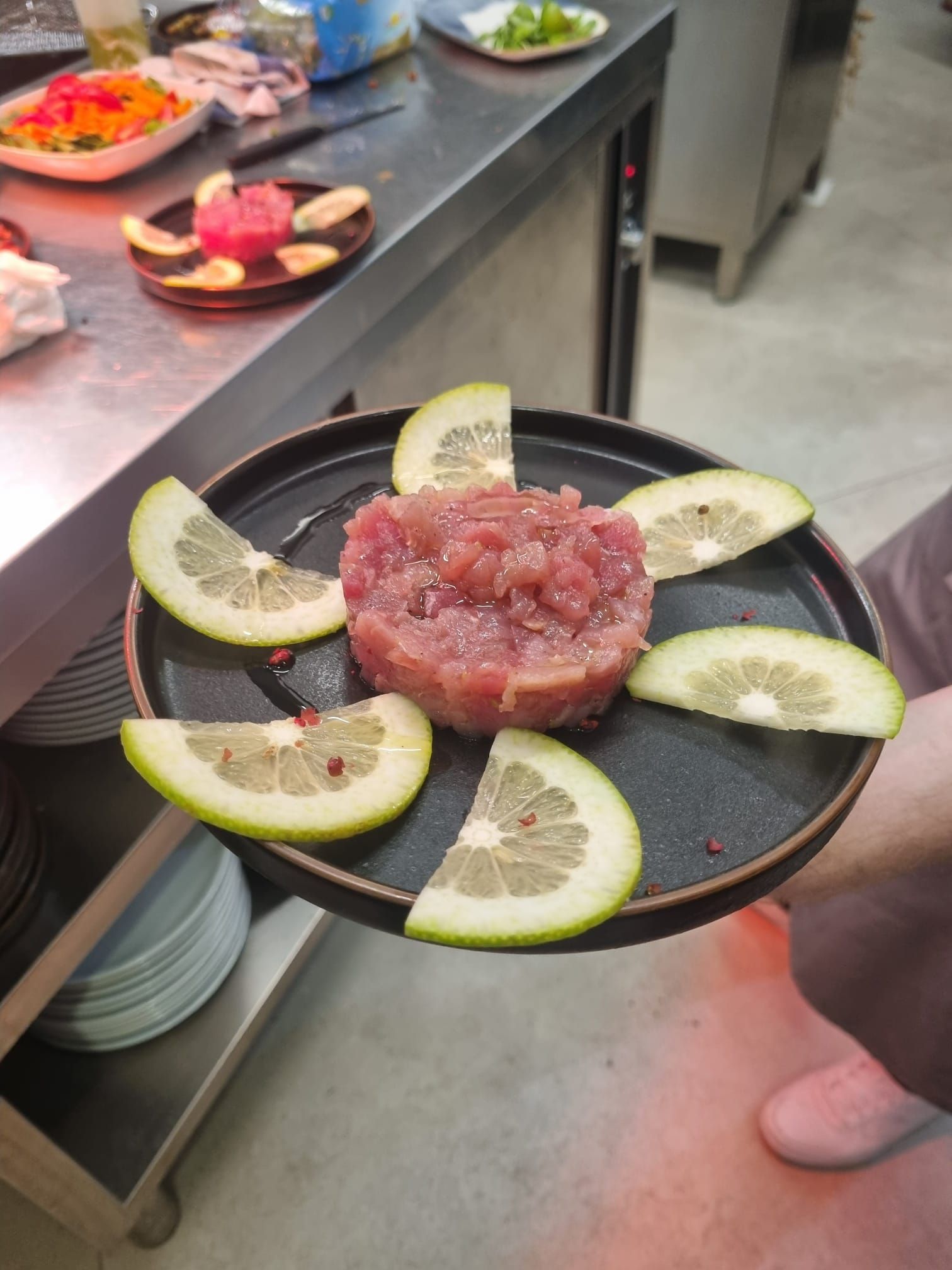 Una persona tiene in mano un piatto con una tartare di pesce rosa, guarnita con fette di pompelmo.