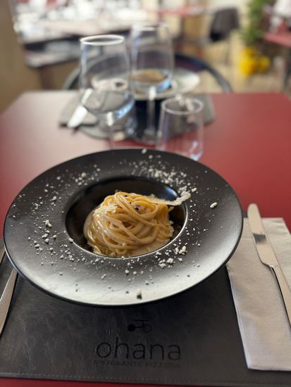 Piatto di pasta in una ciotola nera, su un tavolo rosso. Bicchieri, coltello e forchetta a lato. Tovaglietta 