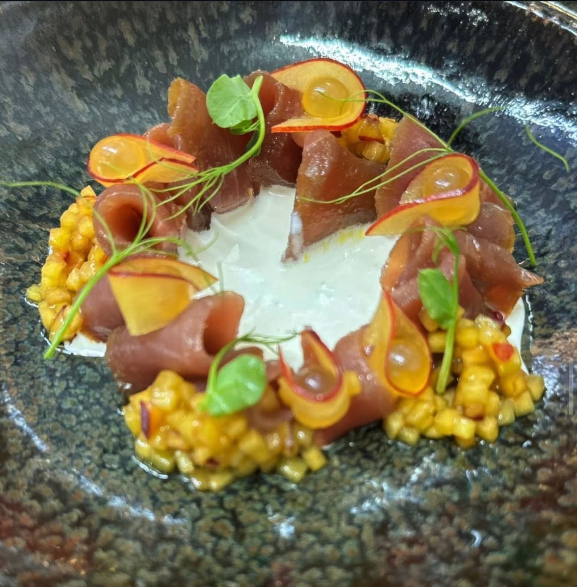 Piatto di tonno su un piatto strutturato: fette di tonno, fette di mela, microgreens, mais e salsa bianca.