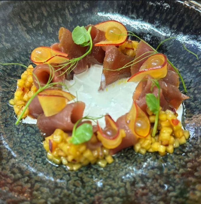 Piatto di tonno su un piatto strutturato: fette di tonno, fette di mela, microgreens, mais e salsa bianca.