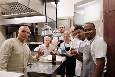 Un gruppo di persone in cucina brinda con bevande. Uomini e donne festeggiano, sorridendo.