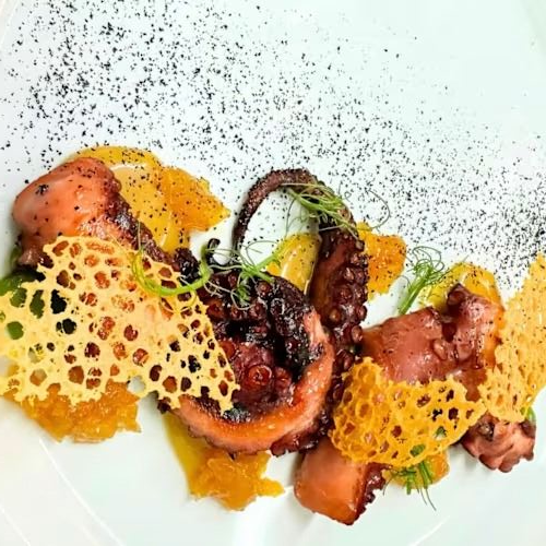 Polpo alla griglia con fette d'arancia e guarnizione di formaggio croccante.