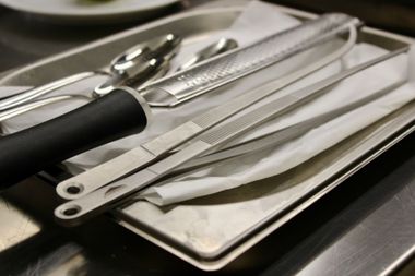 Utensili da cucina in acciaio inossidabile (pinze, cucchiai, coltello) in un vassoio di metallo su un piano di lavoro.