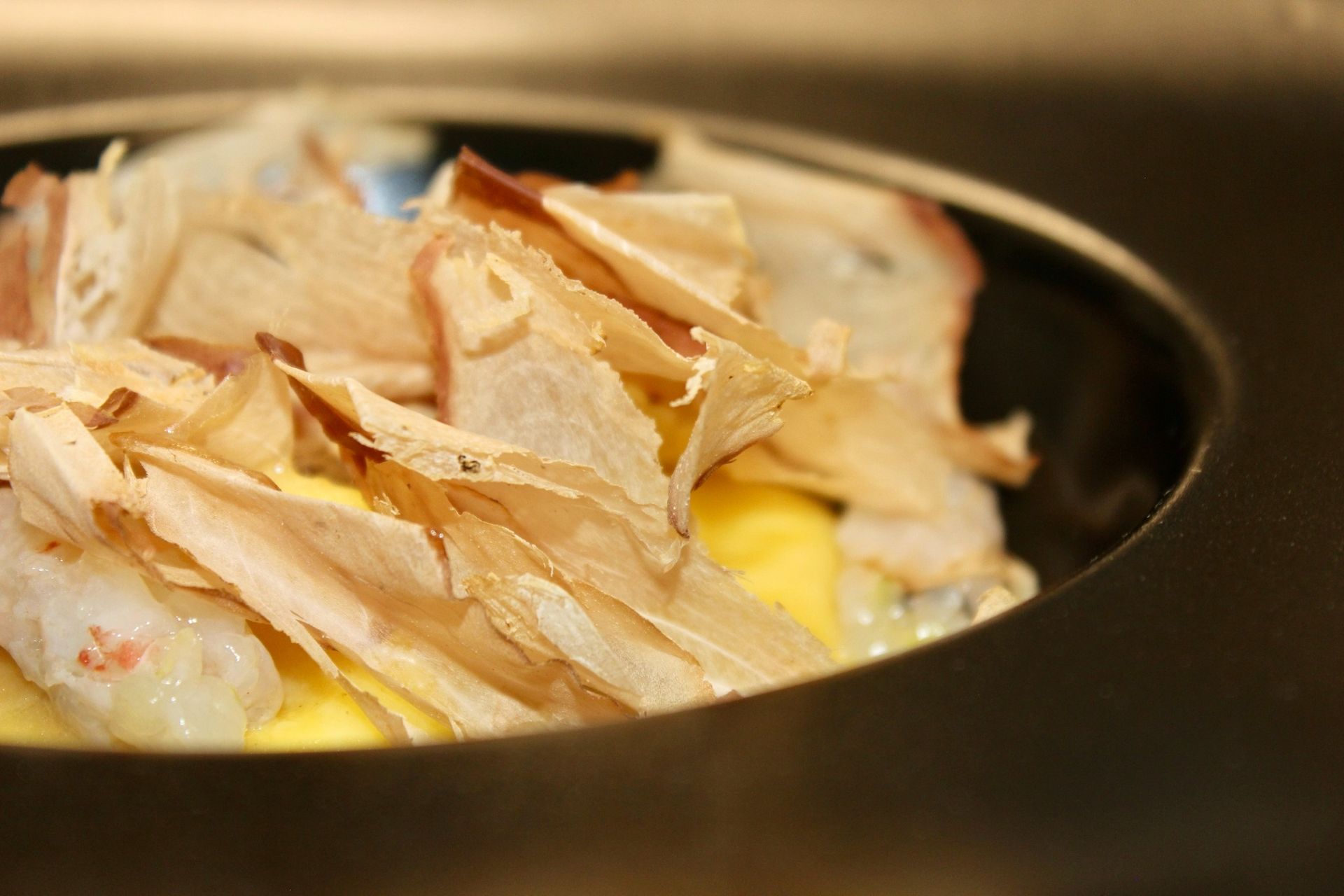 Primo piano di un piatto con salsa gialla, guarnito con frutti di mare bianchi e pezzi marroni grandi, sottili e sfogliati.