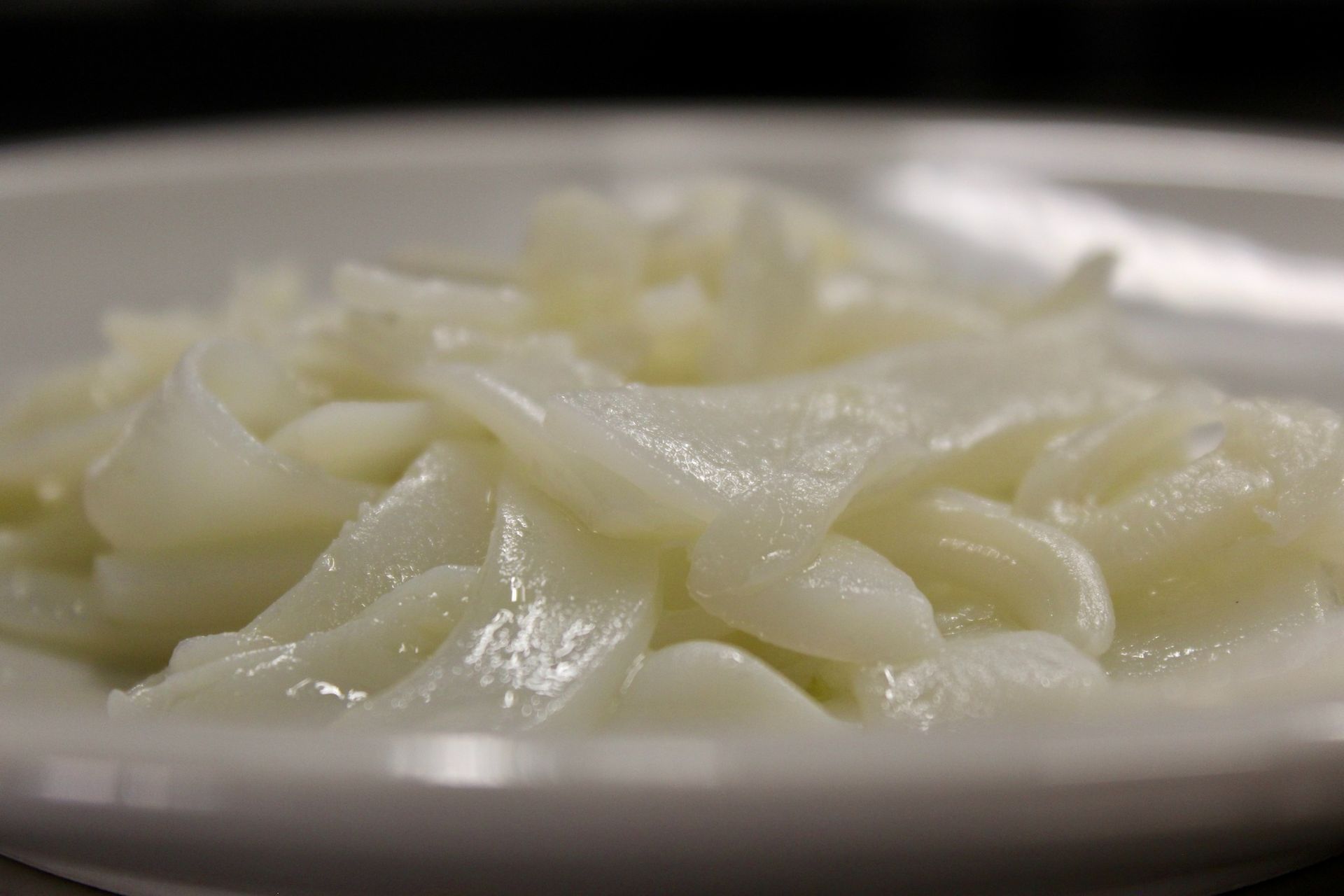 Primo piano di un piatto bianco pieno di calamari luccicanti, tagliati a fette e cotti.
