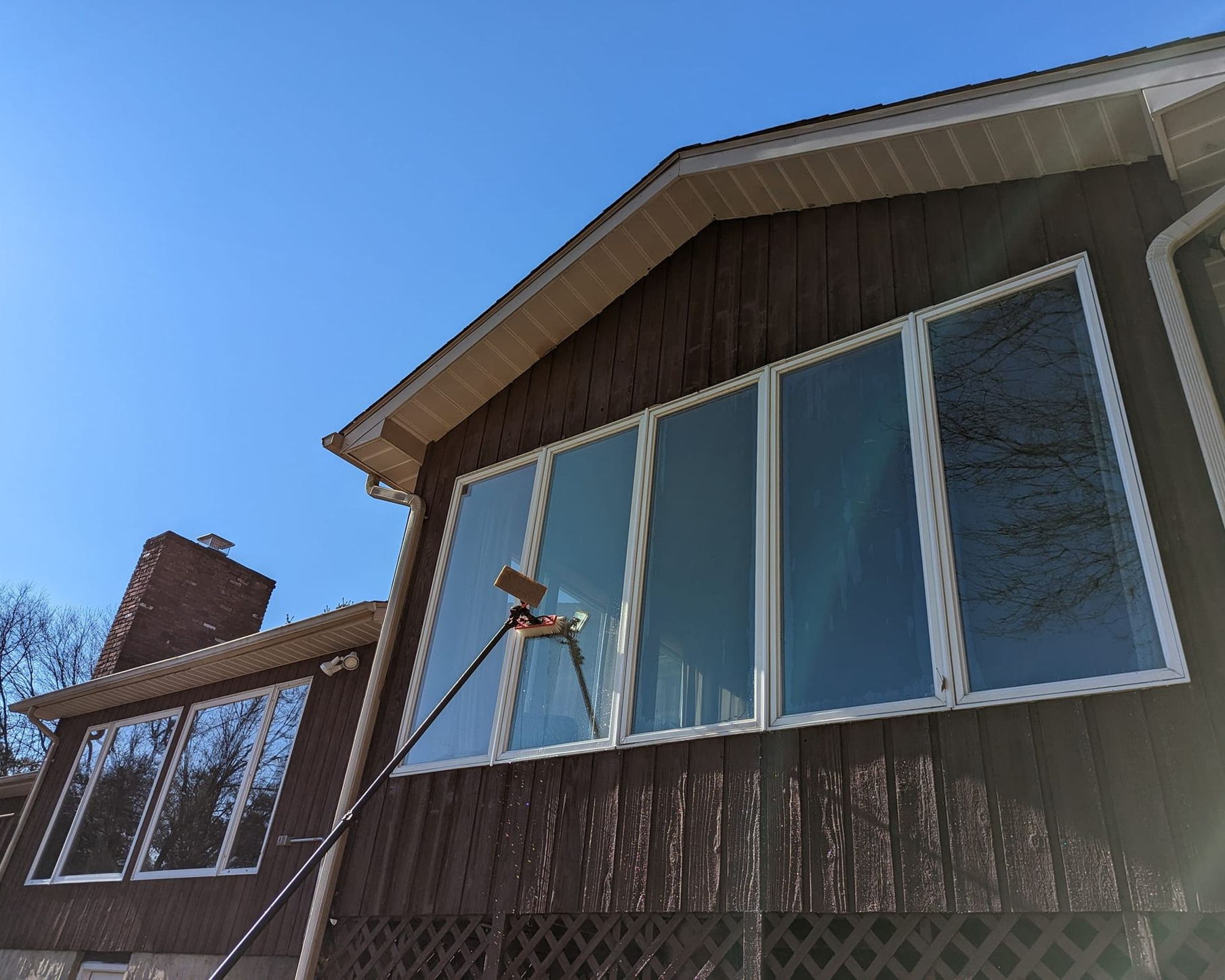 Window cleaner washing windows on a brown house with a blue sky background.