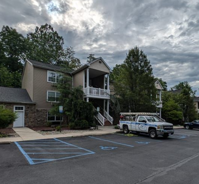 Multi-story building with a covered porch and parked service truck in front; blue parking spaces.