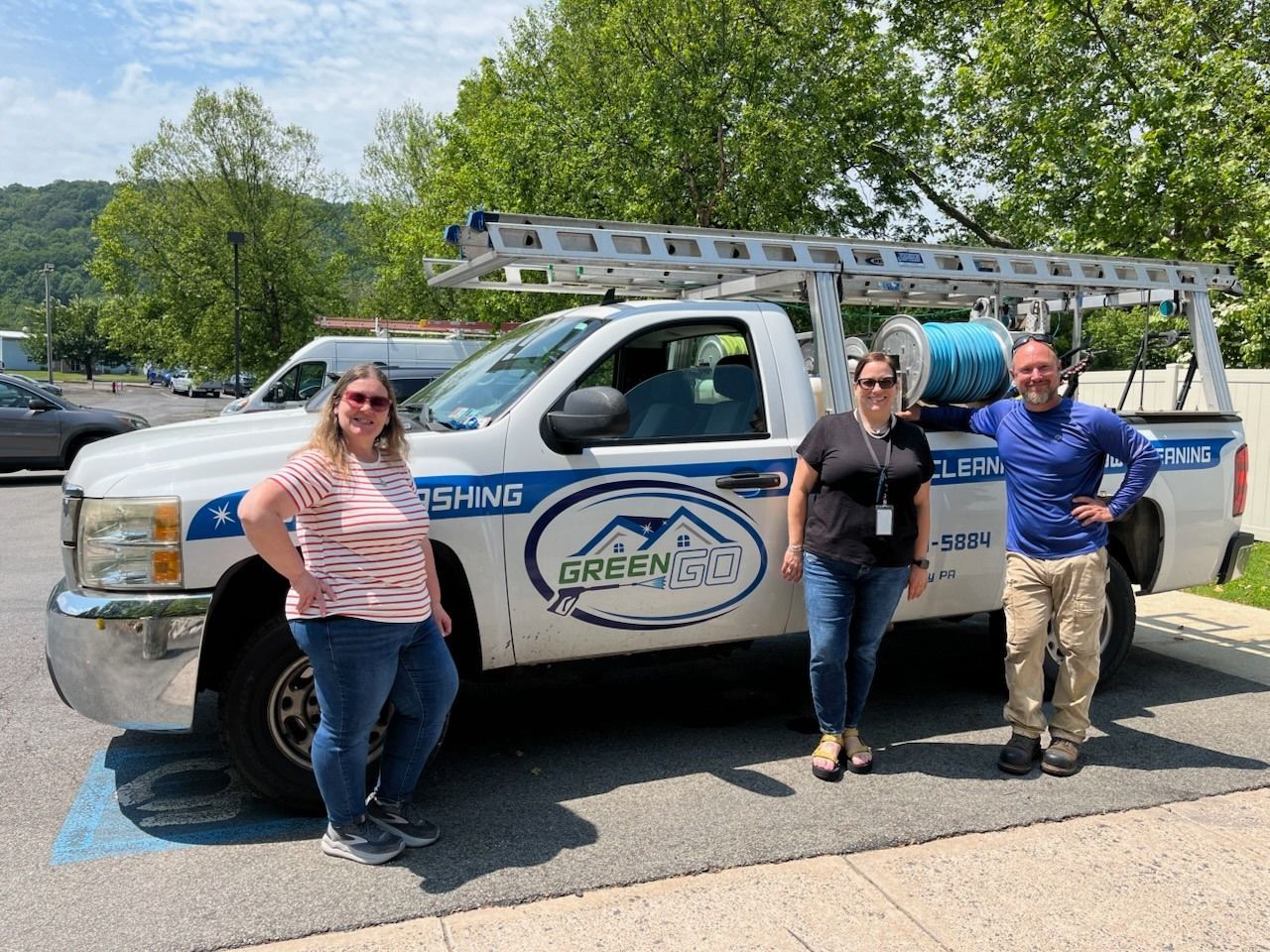 Three people pose beside a white work truck with ladder and company logo