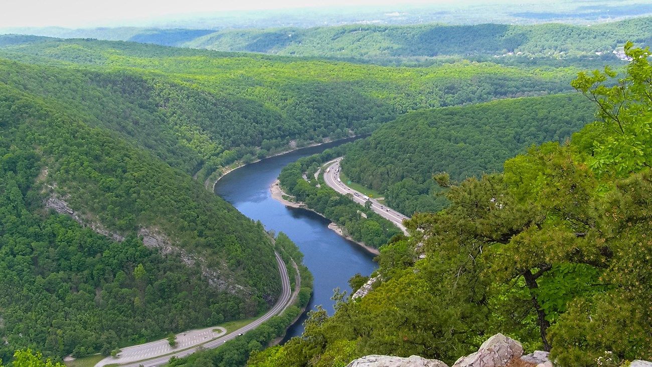 A winding river flows through a lush green valley, with roads visible along its banks.