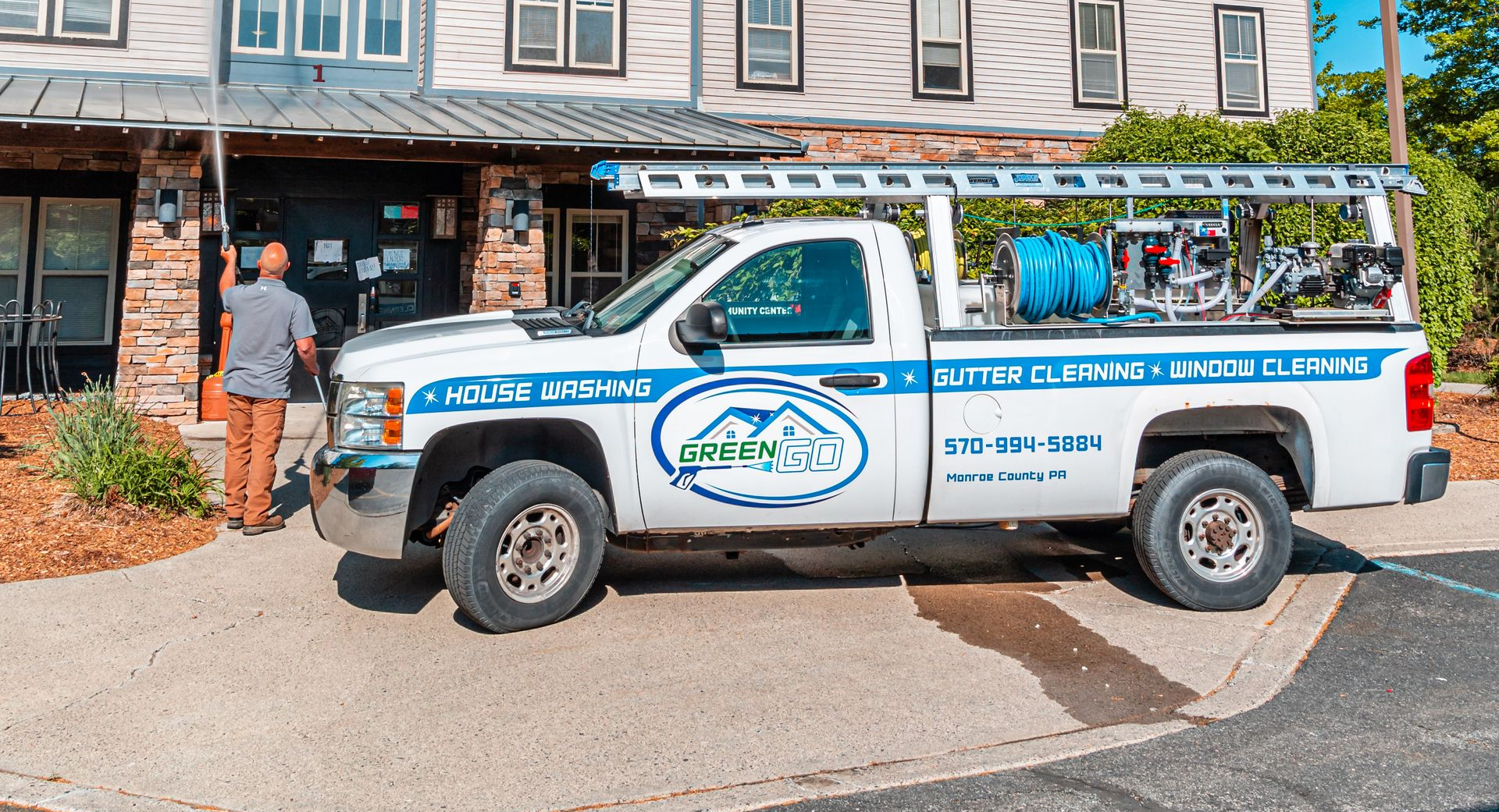 White truck with ladder parked in front of a building. Man stands near door. 