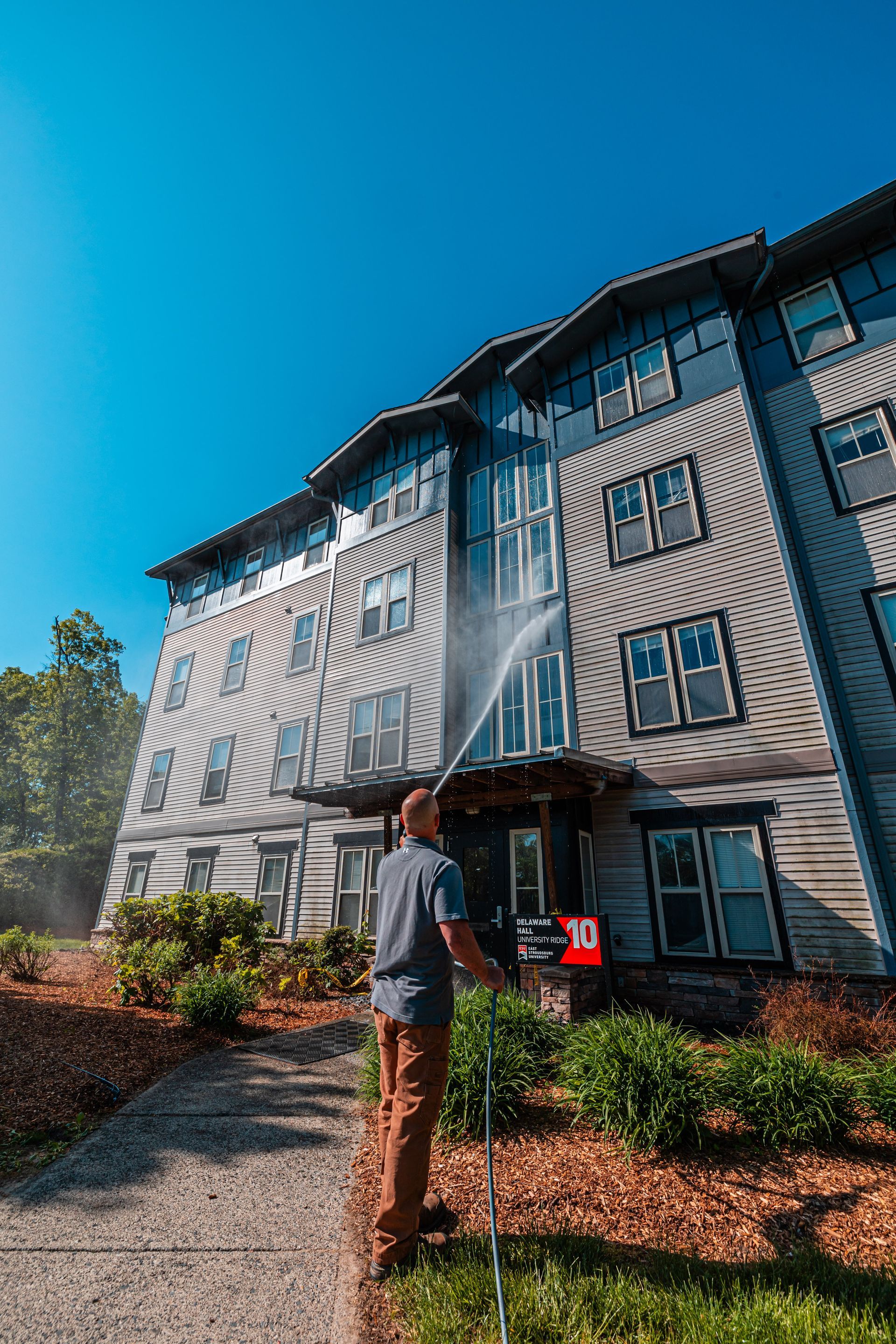 Man power washing a multi-story building on a sunny day.