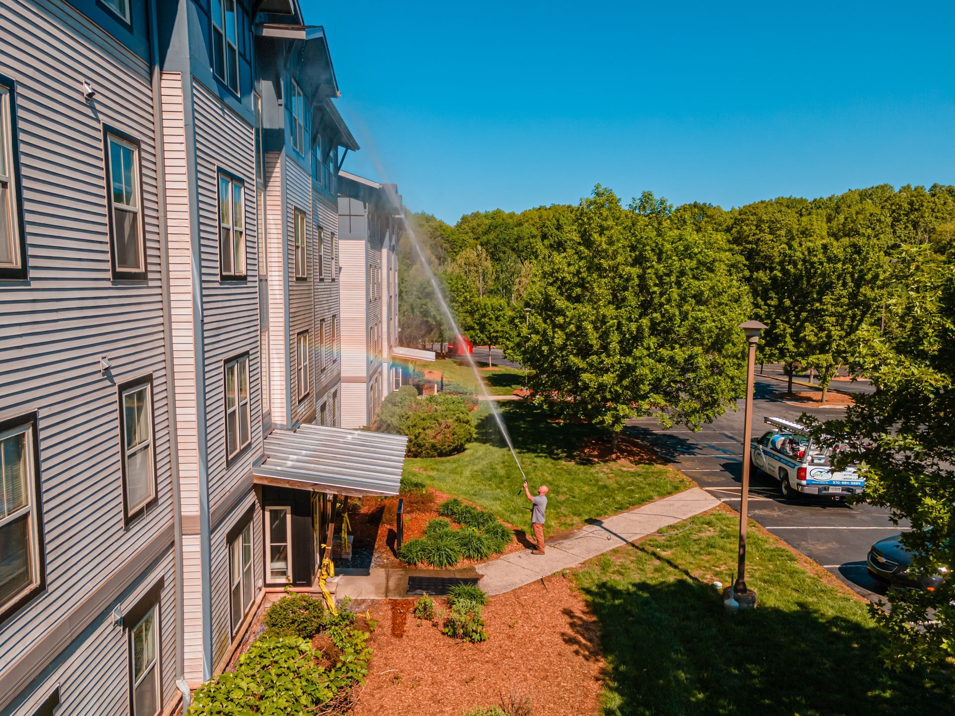 Person power washing a multi-story building exterior. Sunny day.