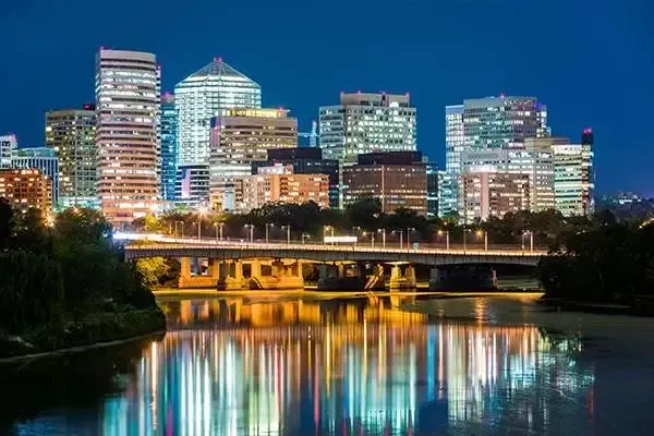 Night view of Arlington, Virginia skyline reflecting in the river, with a bridge in the foreground.