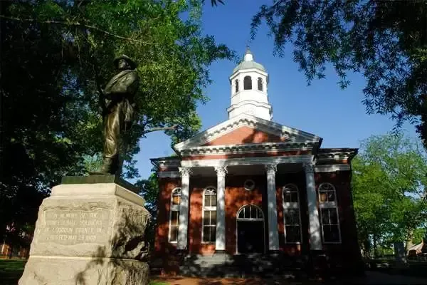 Statue of a soldier beside a red brick courthouse with white columns and a cupola. Trees surround the building.