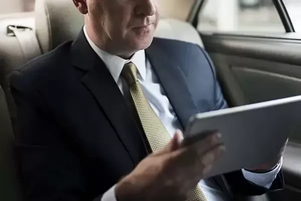 Man in suit in car, looking at tablet.
