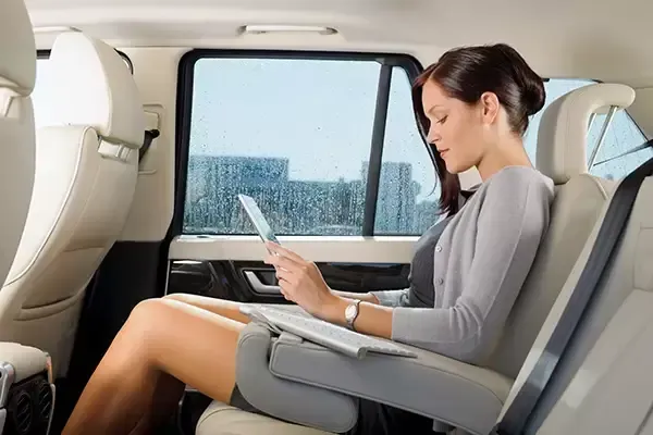 Woman in back seat of a car looking at a tablet, gray cardigan, white leather seats, city outside the window.