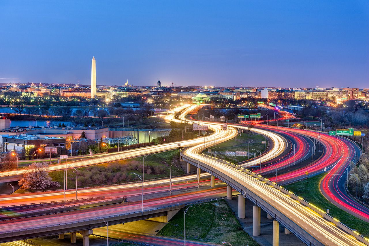 City skyline at dusk with highway traffic light trails. Washington Monument visible.