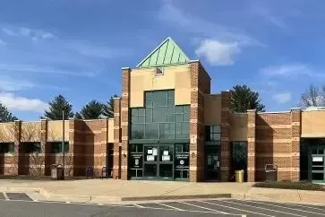 Exterior view of a brick building with a central, multi-level entrance. Green roof, clear sky.