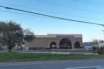 Building with arched entryway and signage; outdoors, daytime. Brown facade, blue sky, power lines overhead.