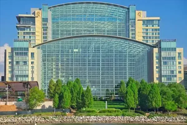 Large modern building with a glass facade and arched roof, overlooking a green space and water.