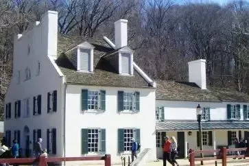 Two white historic buildings with green shutters and chimneys, people walk nearby.