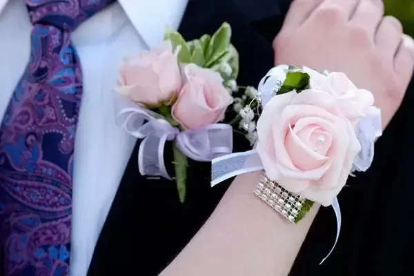 Wrist corsage of pink roses on a person's wrist; tie visible.