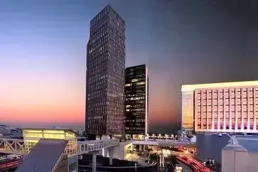 Skyscrapers at dusk with bridge connecting buildings, orange and blue sky, and city lights.
