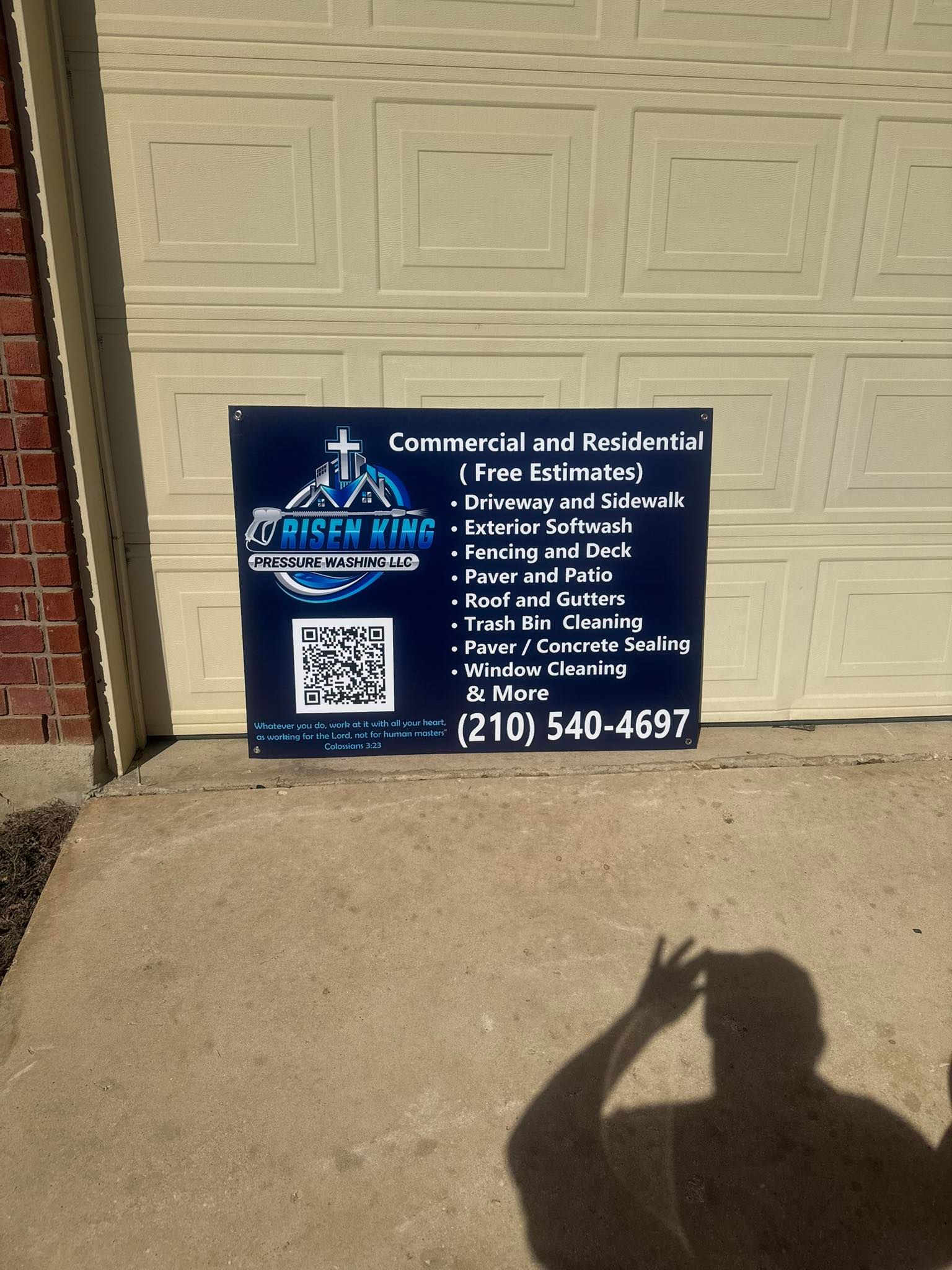A business sign for Risen King Services featuring services, a QR code, and the phone number (210) 540-4697 on a driveway.