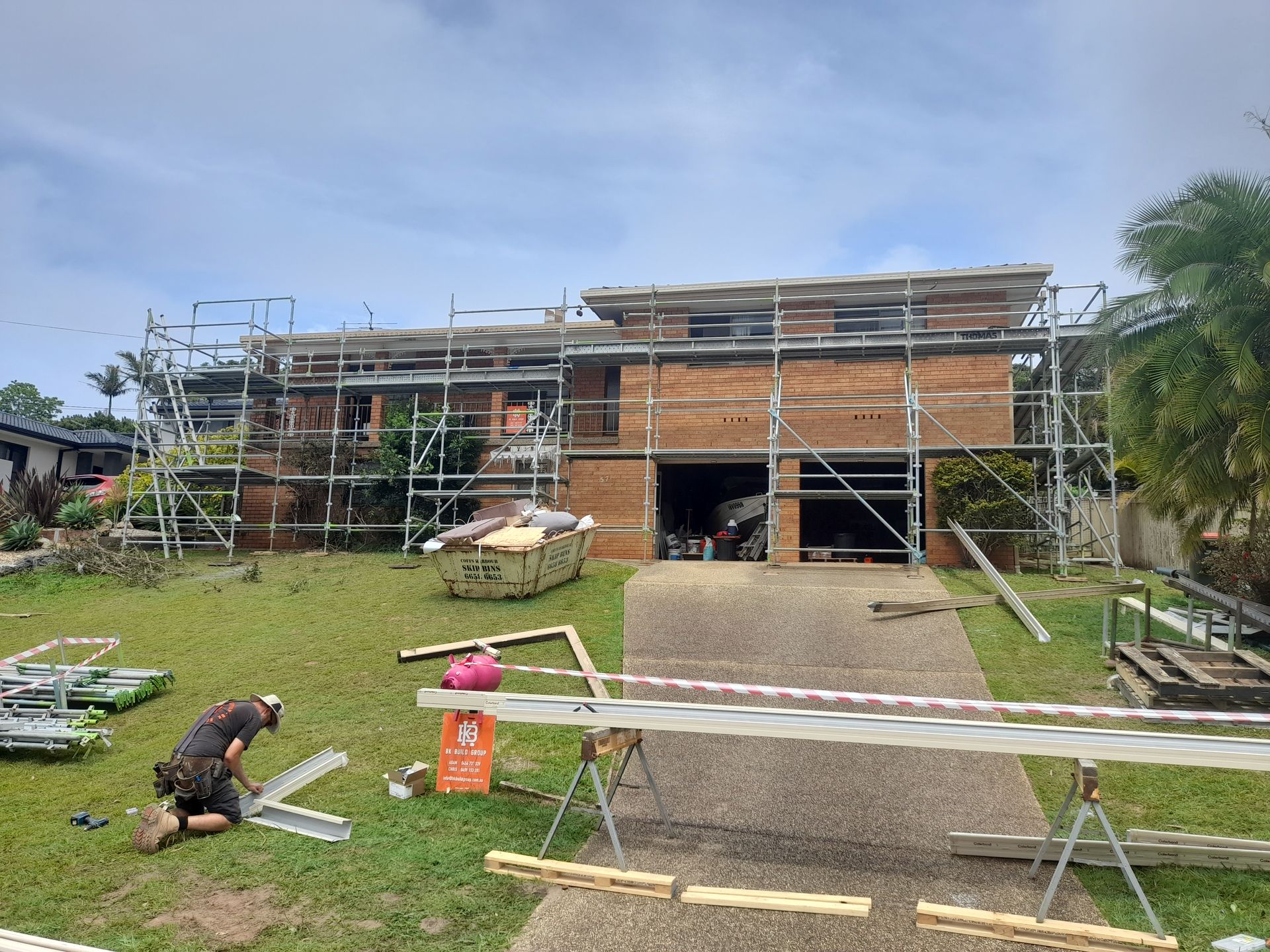 A Man is Kneeling in Front of a House With Scaffolding Around It — BK Build Group in Coffs Harbour, NSW