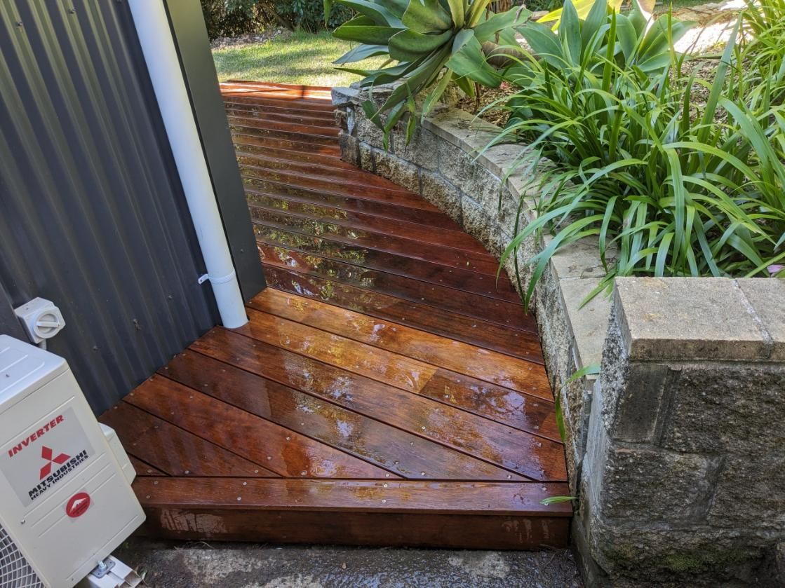 A Wooden Walkway Leading to a House Next to a Brick Wall — BK Build Group in Sawtell, NSW