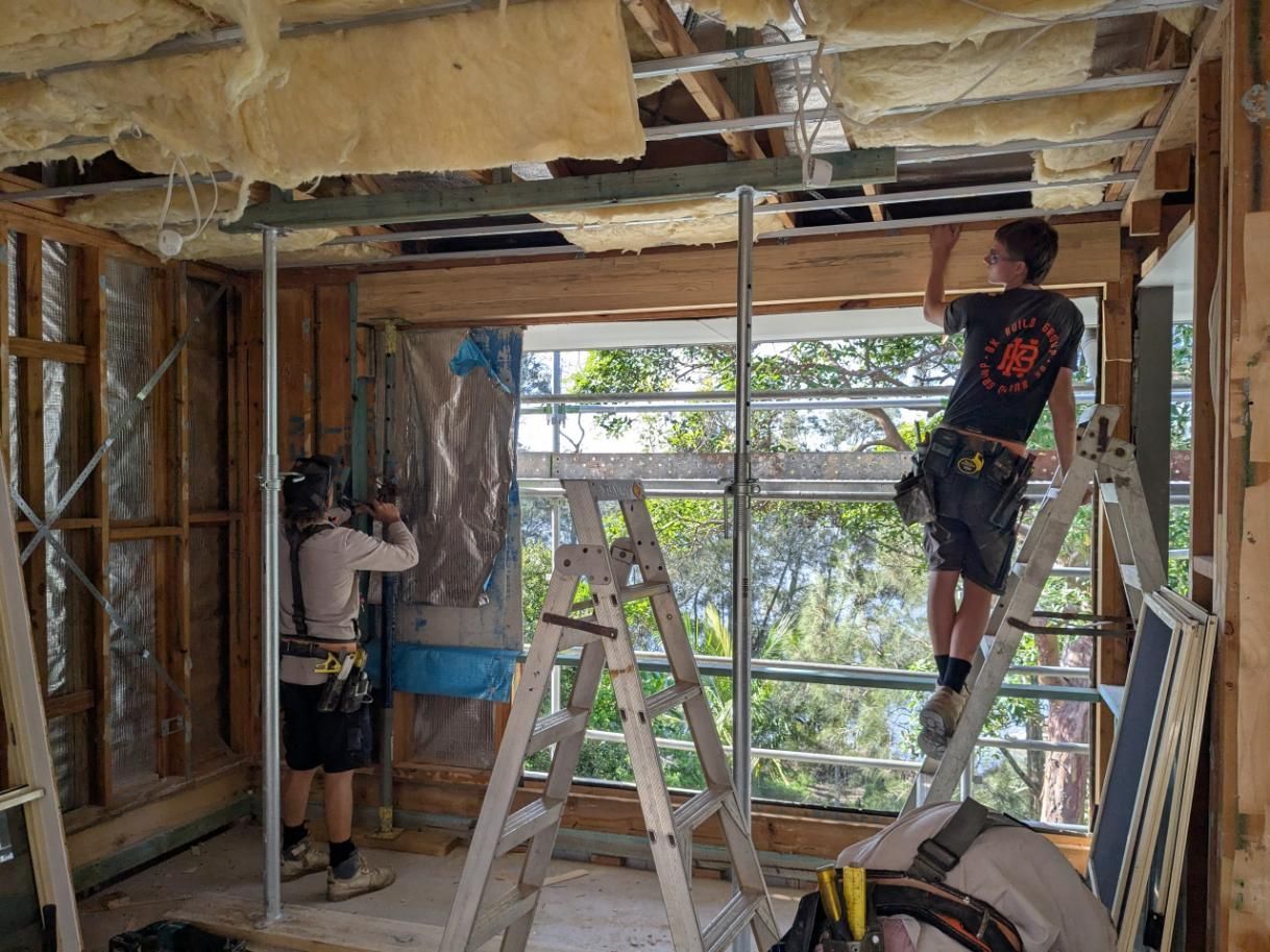 A Man is Standing on a Ladder in a Room Under Construction — BK Build Group in Coffs Harbour, NSW