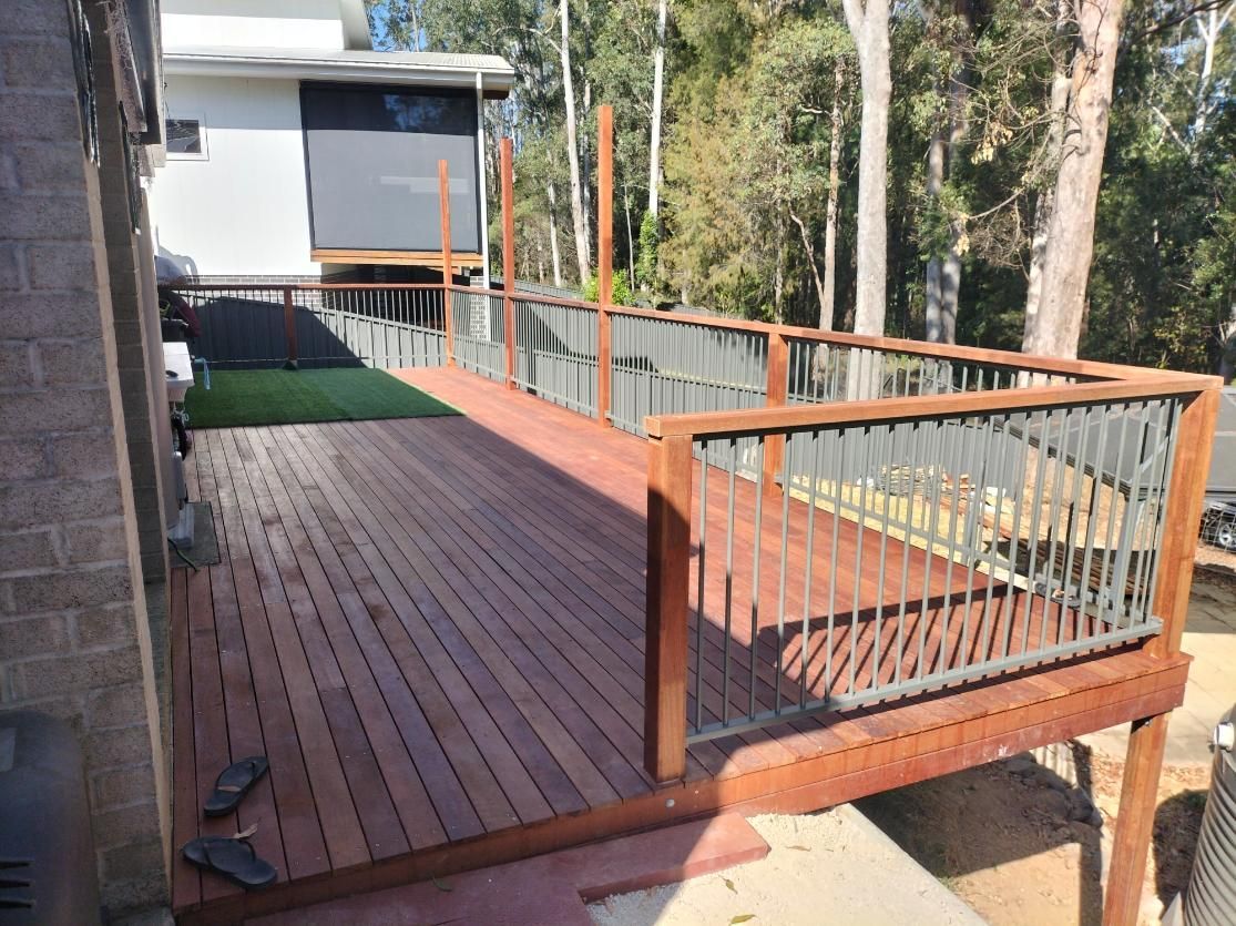 A Wooden Deck With a Metal Railing and a House in the Background — BK Build Group in Woolgoolga, NSW