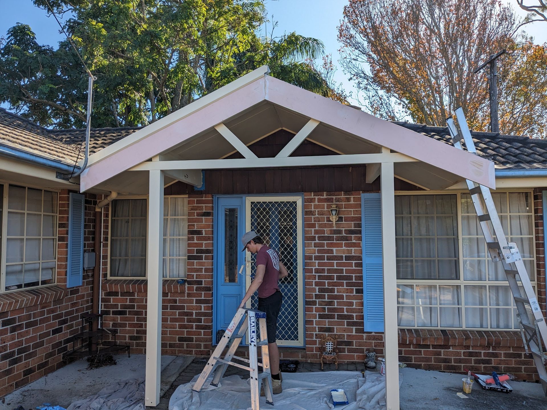 A Man Standing on a Ladder in Front of a Brick House — BK Build Group in Coffs Harbour, NSW