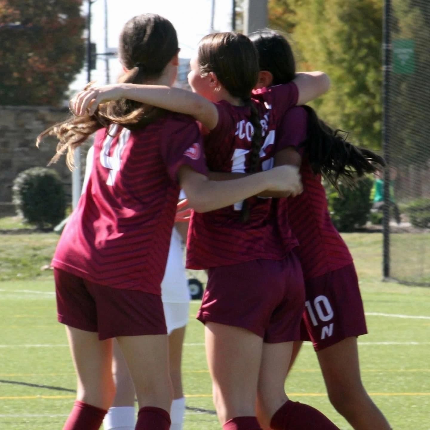 A group of female SCOR soccer players are hugging each other and one of them has the number 10 on her shorts
