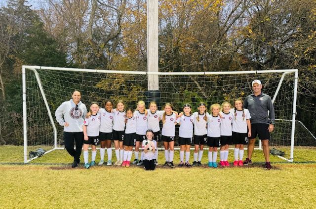 A group of young girls are posing for a picture in front of a soccer goal.