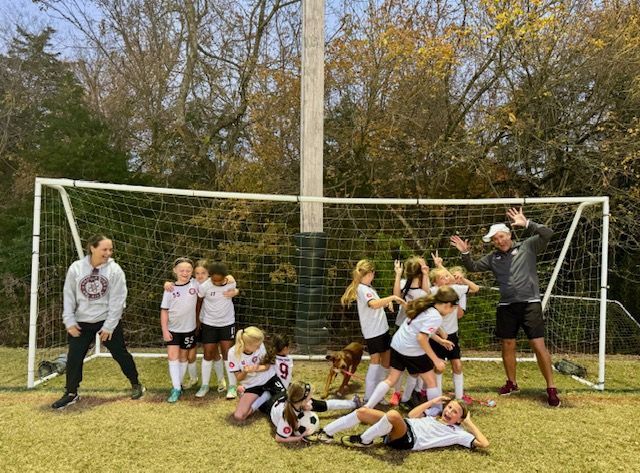 A group of young girls are posing for a picture on a soccer field.