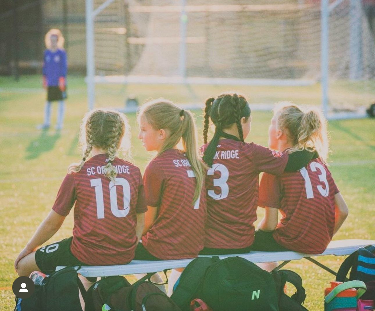 A group of young girls are sitting on a bench on a soccer field.