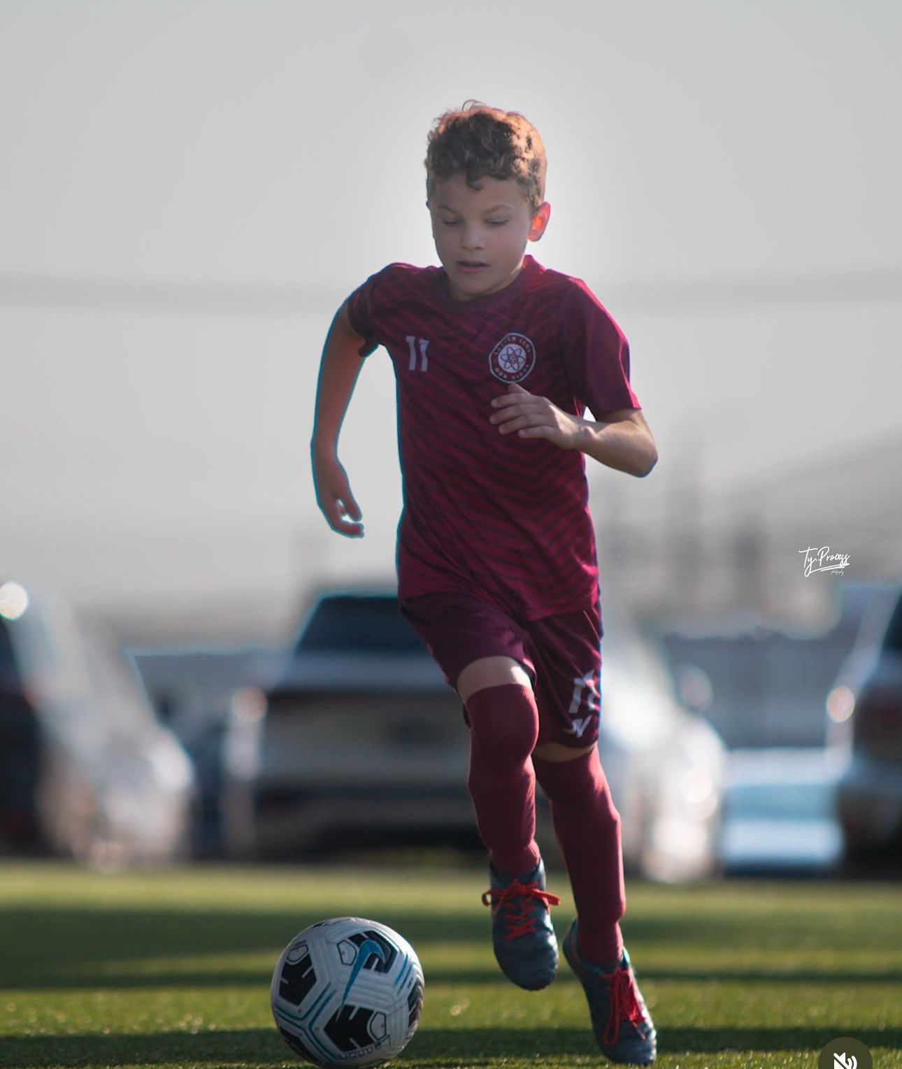 A young SCOR boy is running after a soccer ball on a field.