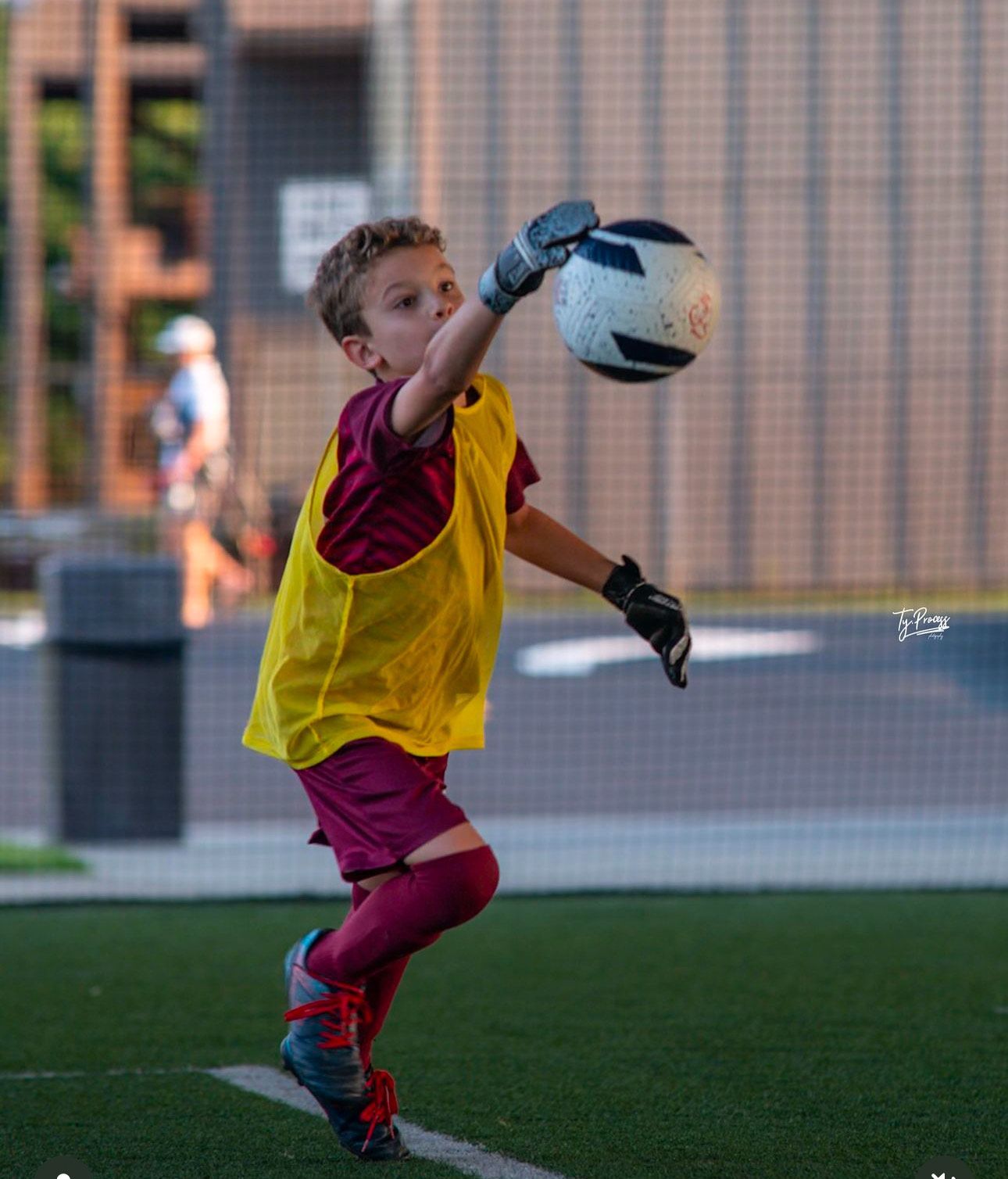 A young boy in a yellow vest is catching a soccer ball