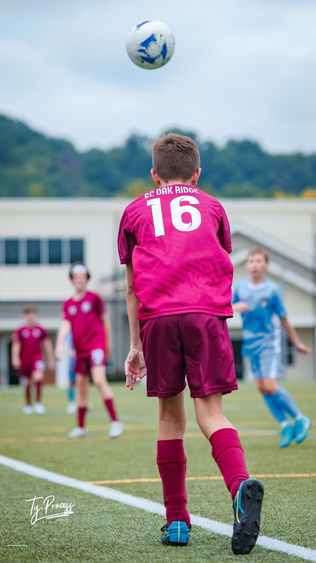 A young boy in a pink jersey with the number 16 on it is kicking a soccer ball.