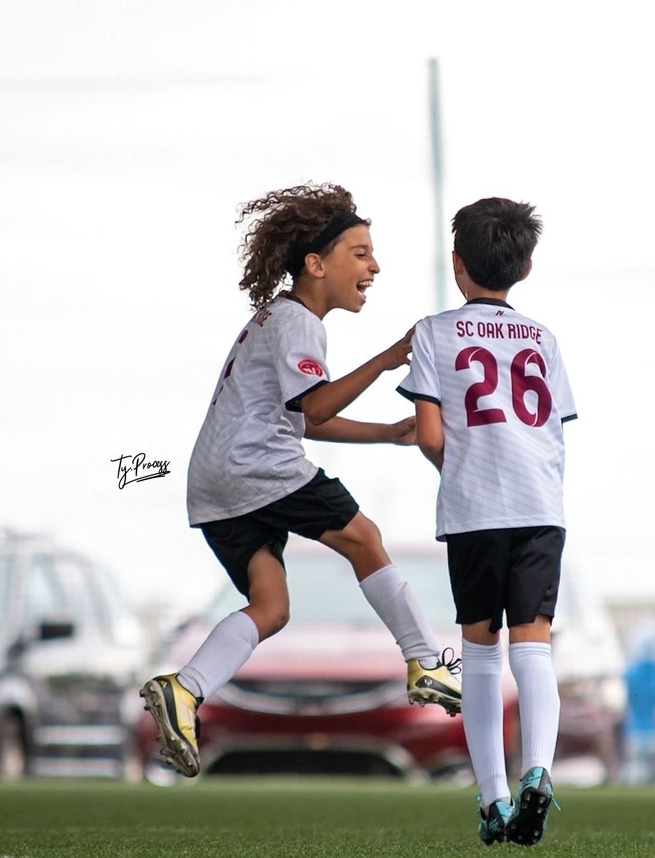 Two young SCOR boys are playing soccer and one of them has the number 26 on his shirt.