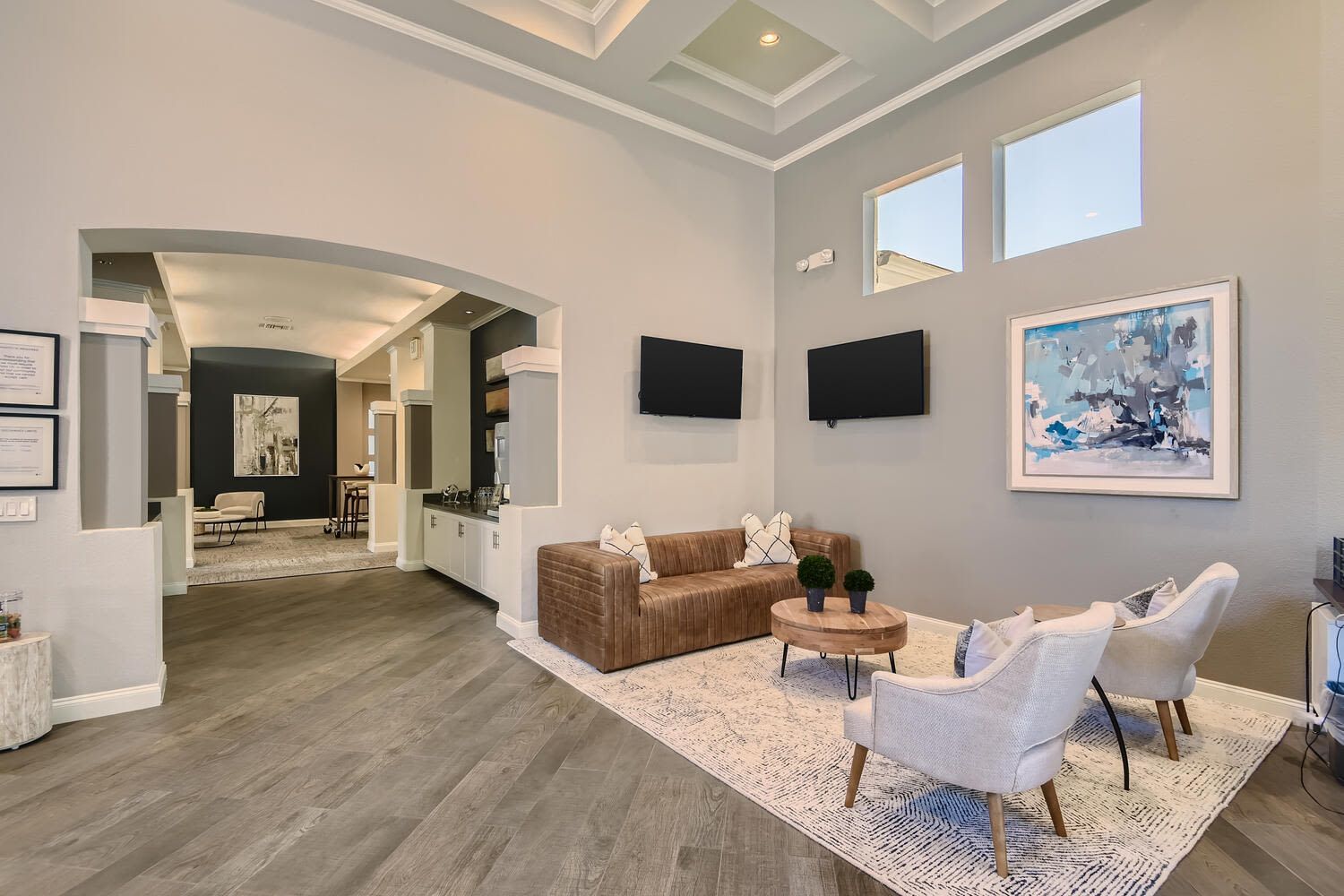 Modern apartment lobby with arched entry, two mounted TVs, and seating area.